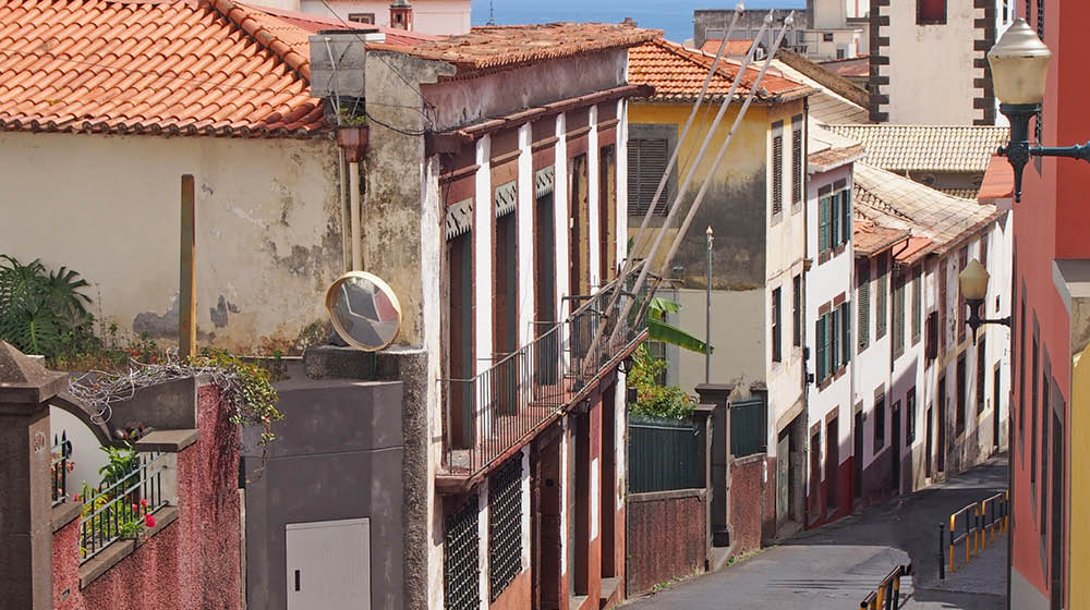 Cal ada de Santa Clara a street of old painted houses in funchal madeira running downhill towards the sea with the historic church of S o Pedro