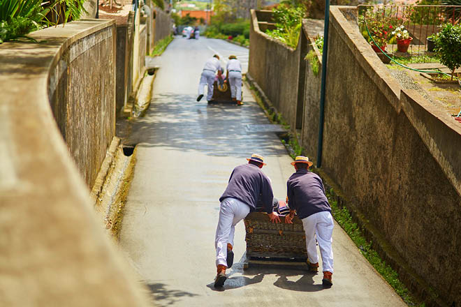 Famous fun tourist activity in Funchal, Madeira island, Portugal. Toboggan riders pushing wooden sledge with tourists downhill with high speed
