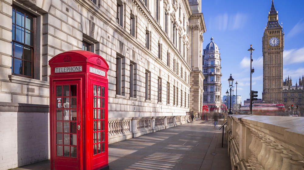 Traditional red british telephone box with Big Ben and Double Decker bus at the background on a sunny afternoon with blue sky and clouds - London, UK