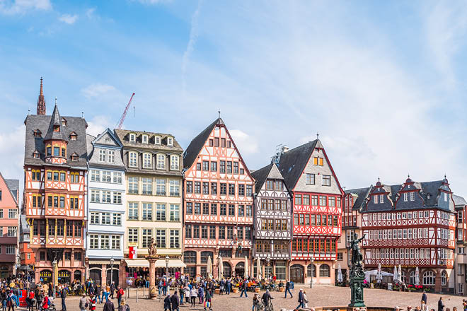 Crowds of tourists in the Romerberg square overlooked by the medieval townhouses, cafes and restaurants of the Altstadt Old Town and spire of Alte Nikolaikirche in the heart of Frankfurt, Hesse, Germany.