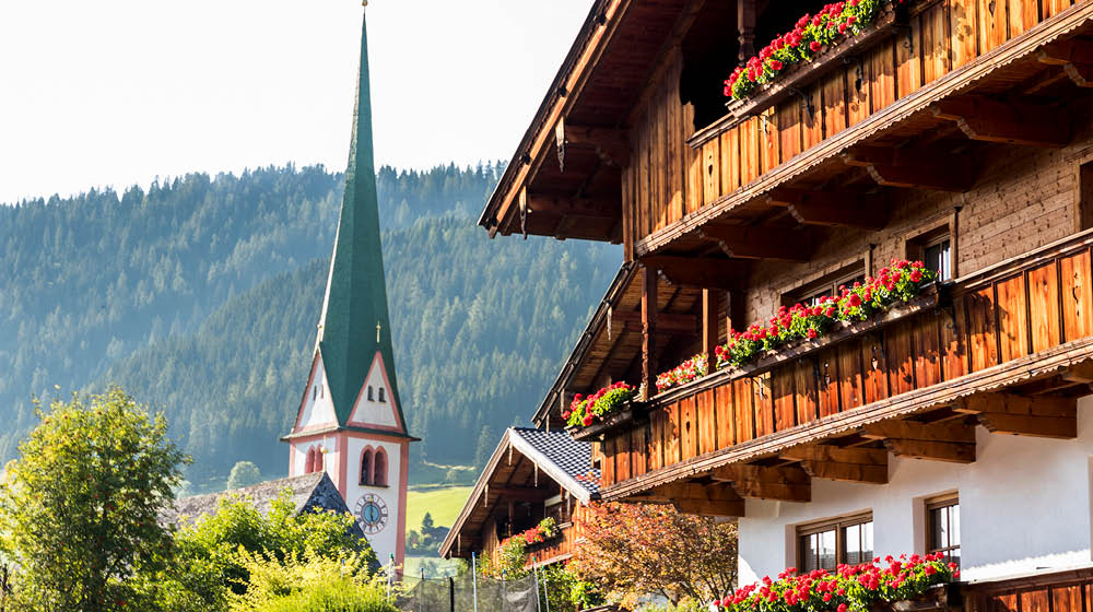 The Saint Oswald Parish Church and a typical wooden balcony with flowers in Alpbach, a town in western Austria in the state of Tyrol