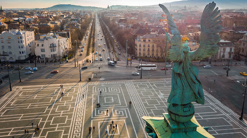 Budapest, Hungary - Angel sculpture from behind on the top of Heroes' Square at sunset with Andrassy street and the skyline of Budapest at background