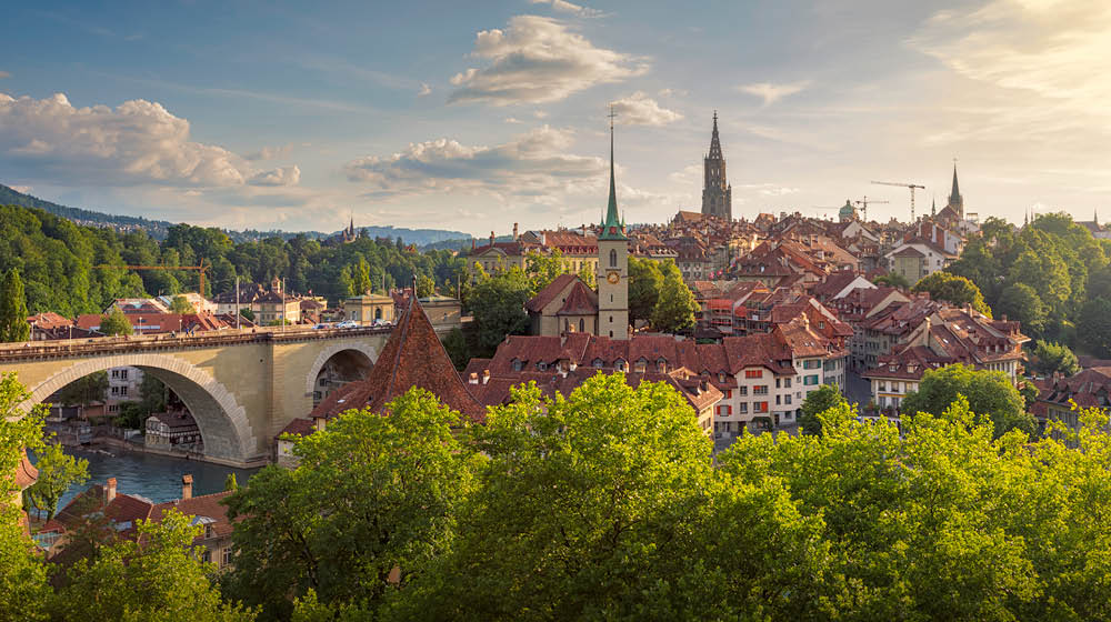 View of the city of Bern on a summer evening. On the left is the Nydeggbr cke (bridge), and the towers belong to the Nydeggkirche (church) and Berner M nster (Cathedral of Bern).