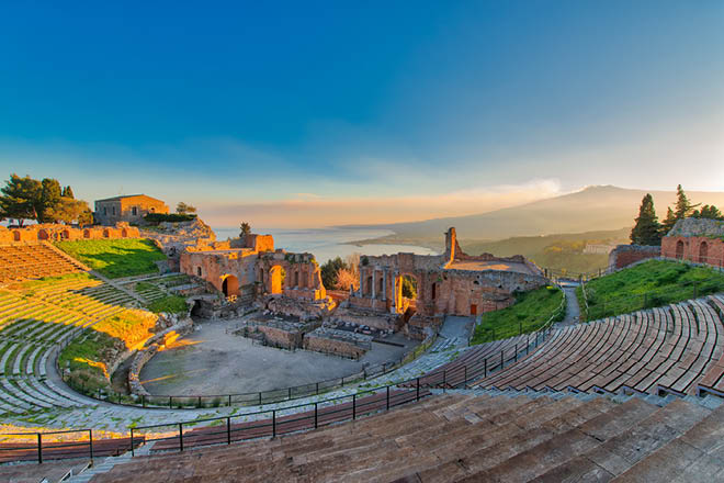 Ancient theatre of Taormina Siciliy Italy with Etna erupting volcano at sunset