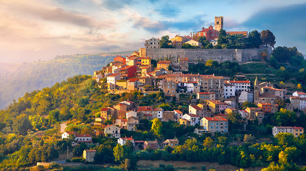 Antique city Motovun Croatia Istria. Picturesque panorama age-old village at hill with pink cloud and sunny light and authentic home with red tegular roof and green vineyard garden.