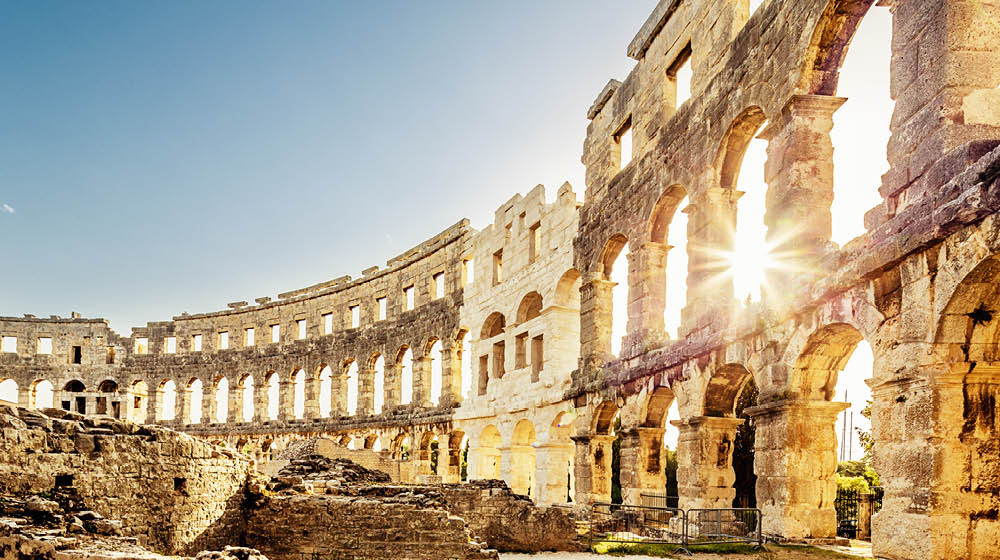 Roman Amphitheater in Pula Croatia. Built during 1st century AD, the amphitheater is the sixth largest in the world and has well preserved outer walls. Interior view with sun shining through arches into the roman colosseum. City of Pula, Croatia.