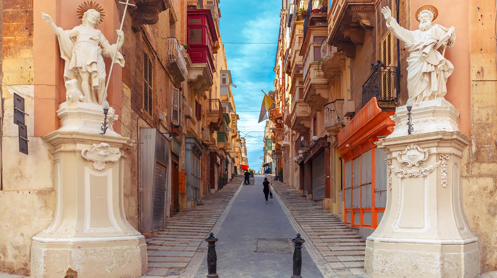 The traditional Maltese street stairs with corners of houses, decorated with statues of saints St. John and St. Paul and building with colorful balconies in Valletta, Capital city of Malta