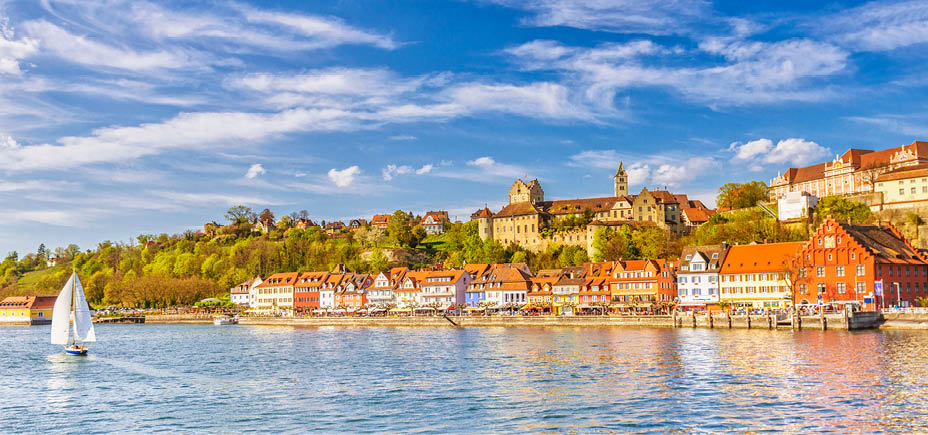 Panoramic view on the charming medieval city of Meersburg, located at the Lake Constance (Bodensee), with a sailing boat passing the city´s beautiful waterfront in the lower town and it´s landmark castles in the upper town. 