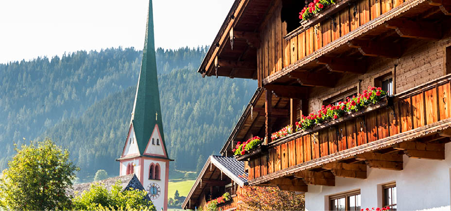 The Saint Oswald Parish Church and a typical wooden balcony with flowers in Alpbach, a town in western Austria in the state of Tyrol