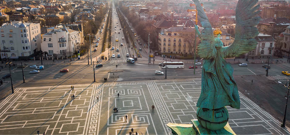 Budapest, Hungary - Angel sculpture from behind on the top of Heroes' Square at sunset with Andrassy street and the skyline of Budapest at background