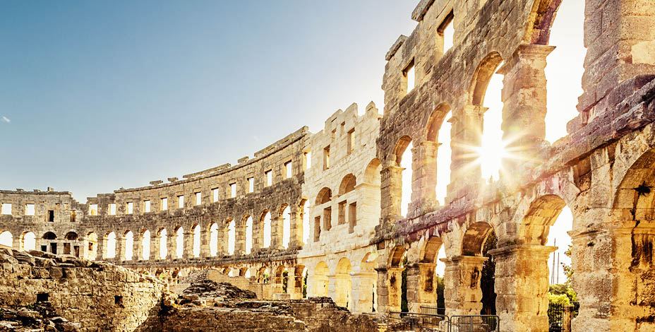 Roman Amphitheater in Pula Croatia. Built during 1st century AD, the amphitheater is the sixth largest in the world and has well preserved outer walls. Interior view with sun shining through arches into the roman colosseum. City of Pula, Croatia.